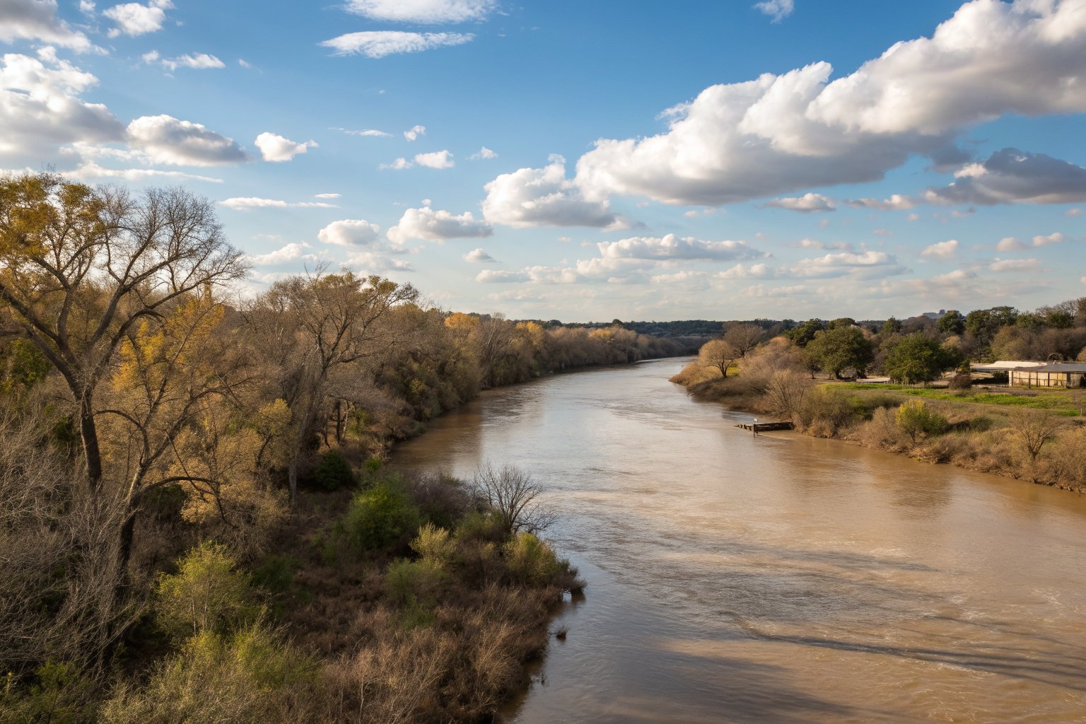 Wide, muddy river curving between low wooded banks under a big blue sky